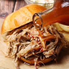 someone pouring barbecue sauce onto a pulled pork sandwich