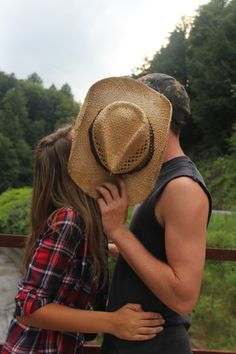 a man in a cowboy hat kissing a woman's face on the bridge over a river