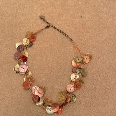 a multi - stranded necklace with buttons and chains on the bottom is laying on the floor