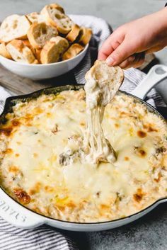 a hand holding a tortilla chip over a skillet filled with cheese and bread