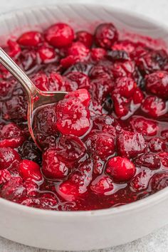 a white bowl filled with cranberry sauce on top of a counter next to a silver spoon