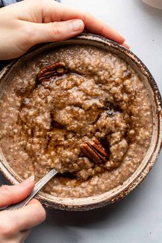 two hands holding a bowl of oatmeal with pecans