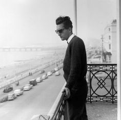 a black and white photo of a man standing on a balcony looking at the street