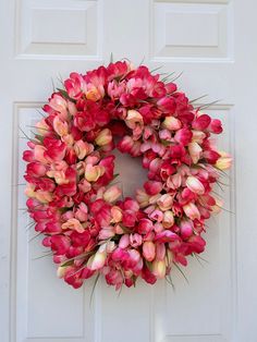 a wreath with pink tulips hanging on a white door, in front of a white paneled door