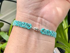 a woman's arm with a turquoise beaded bracelet on it and a plant in the background