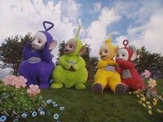 three inflatable characters are sitting on the grass with flowers and trees behind them