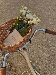 a basket on the back of a bicycle with flowers in it and a book sitting inside