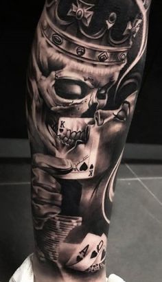 a man's leg with a skull wearing a crown and playing cards on it