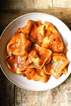 a white bowl filled with pasta and sauce on top of a wooden table next to a fork