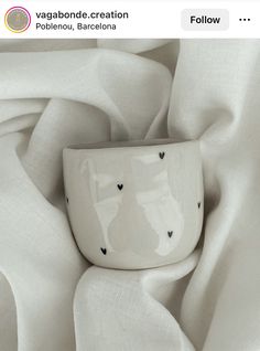 a white cup sitting on top of a table covered in sheets and cloths with hearts drawn on it