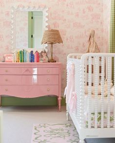 a baby's room decorated in pink and green with a dresser, crib, mirror and lamp