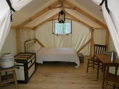 a bed sitting inside of a tent next to a wooden table and two small chairs