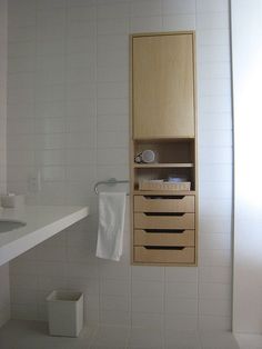 a bathroom with white tile and wooden cabinet above the sink, in front of a mirror