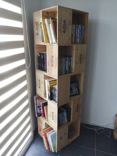 a bookshelf made out of wooden crates filled with books on the floor next to a window