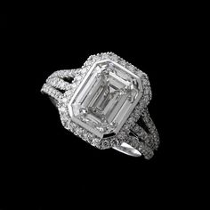 an emerald cut diamond surrounded by diamonds on a black background, with the center stone set in