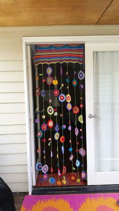 a door decorated with colorful crochet and beads on the front porch, next to a black cat