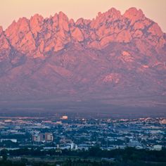 the mountains are covered in snow as seen from an area near city lights and buildings