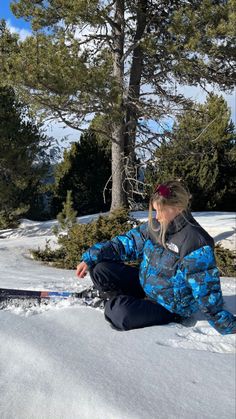 a person sitting in the snow with skis on their feet and trees behind them