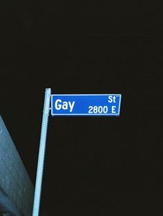 a blue street sign sitting on the side of a road at night time with buildings in the background