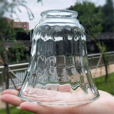 a hand holding a glass bell jar in front of a building with trees behind it