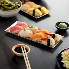 sushi and vegetables on a black table with chopsticks in the foreground