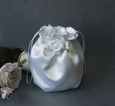 a white satin bag next to flowers on a gray surface with one flower in the middle