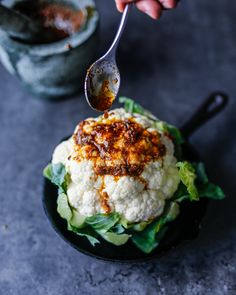 a person is spooning some food out of a black bowl with lettuce and sauce on it