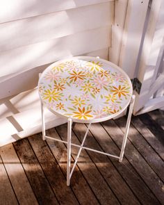 a small white table sitting on top of a wooden floor next to a wall with flowers painted on it