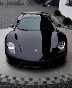 a black sports car parked in front of a building on a cobblestone driveway