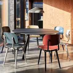 a round table with four chairs around it in front of a wooden wall and windows