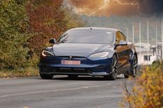 a blue tesla parked on the side of a road in front of trees and lightning