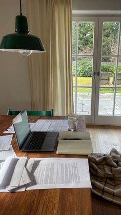 an open laptop computer sitting on top of a wooden table next to books and papers