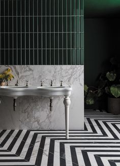 two white sinks sitting on top of a black and white floor next to a green wall