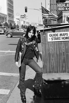 black and white photograph of a woman leaning against a trash can on the side of the road