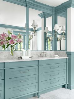 a bathroom with blue cabinets and marble counter tops, two sinks and large mirrors on the wall