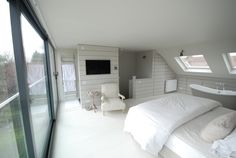 a bedroom with white bedding and windows overlooking the backyard area is pictured in this image