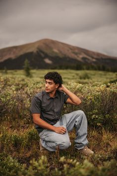 a man sitting in the middle of a field with mountains in the backgroud