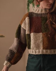 a woman with long hair wearing a multicolored sweater looking down at the ground