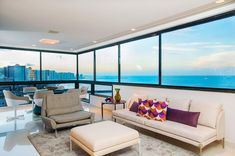 a living room filled with furniture next to large windows overlooking the ocean and cityscape