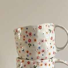 two coffee mugs are stacked on top of each other with colorful flowers painted on them