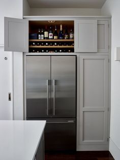 a stainless steel refrigerator in a kitchen with wine bottles on the top shelf and cabinets above it