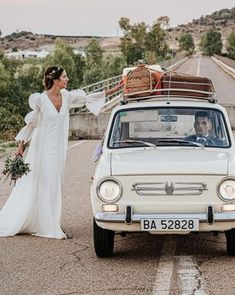 a bride and groom standing in front of an old car with luggage on the roof