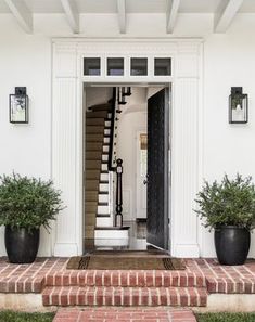 the front door is open and there are potted plants on the steps