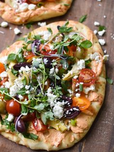 two flatbread pizzas topped with fresh vegetables and feta cheese on a wooden board