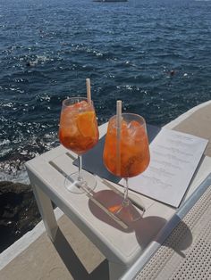 two drinks are sitting on a table near the water