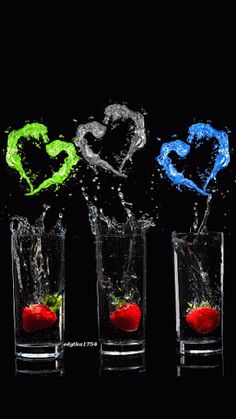 two glasses filled with water and strawberries splashing into each other on a black background