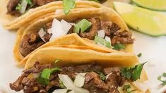 three tacos with meat, onions and cilantro on a plate next to lime wedges