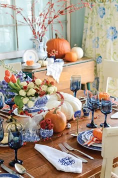 a dining room table is set with blue and white dishes, pumpkins and flowers