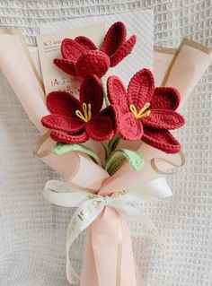 red crocheted flowers are placed on top of a white card and tied to a pink ribbon