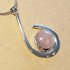 I created this elegant small pendant by hand fabricating Sterling Silver into a wrap around design holding a Pink Rose Quartz Cabachon.  The Rose Quartz is 12 mm round stone.  This piece can be worn casually or in a more formal outfit.  This pendant is about 1-1/2 inches long by 3/4 inch wide.  I am including a Sterling Silver 18 inch long 8 sided Snake Chain so it can be worn  immediately. Modern Round Cabochon Necklace, Modern Cabochon Necklace, Modern Jewelry With Round Cabochon Pendant, Modern Cabochon Round Pendant Jewelry, Modern Cabochon Round Pendant, Modern Cabochon Jewelry, Modern Wire Wrapped Round Jewelry, Modern Round Wire Wrapped Jewelry, Modern Wire Wrapped Jewelry